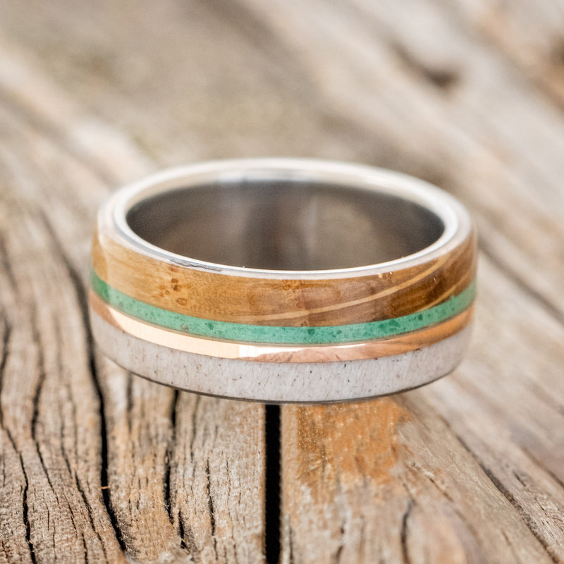 Shown here is "Argos", a custom, handcrafted men's wedding ring featuring whiskey barrel oak and antler overlays with malachite and 14K rose gold inlays, laying flat. Additional inlay options are available upon request.