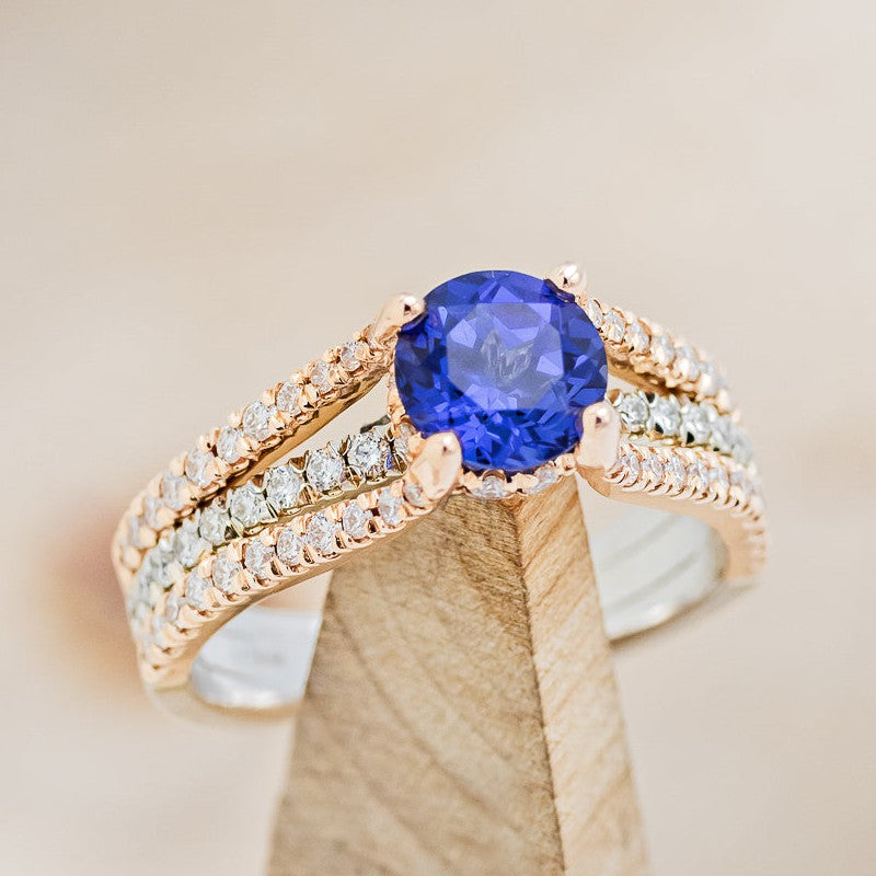 Shown here is The "Roxie", a french set-style lab-created sapphire two-tone women's engagement ring with delicate and ornate details and is available with many center stone options
