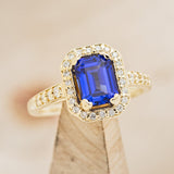 Shown here is The "Karla", a halo-style lab-created sapphire women's engagement ring with delicate and ornate details and is available with many center stone options