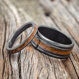 Shown here is a matching wedding band set featuring "Eterna" & "Austin", upright facing left. "Austin" is a handcrafted wide wedding band featuring whiskey barrel inlay. "Eterna" is a stacking-style wedding band featuring whiskey barrel inlay.