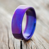 Shown here is a handcrafted men's wedding ring featuring a fire-treated titanium band, upright facing left. 