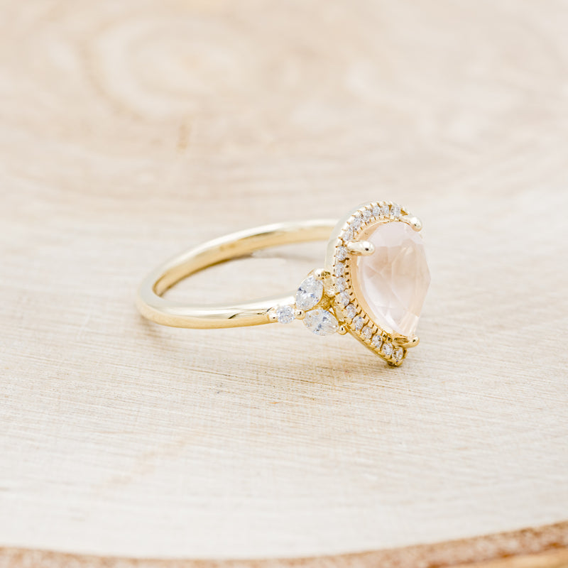 Shown here is "Dream", a rose quartz women's engagement ring with a diamond halo and diamond accents, facing right. Many other center stone options are available upon request.