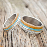 Shown here is a "Banner" matching set is a custom, handcrafted matching set of wedding rings featuring elk antler, turquoise, whiskey barrel oak, and 14K yellow gold inlay, upright facing left. Additional inlay options are available upon request.