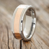 Shown here is a custom, handcrafted men's wedding ring featuring a 14K rose gold inlay on a tungsten band, upright facing left. Additional inlay options are available upon request.