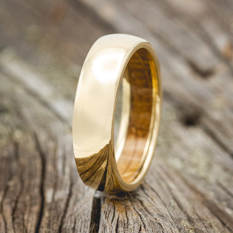 Shown here is a handcrafted men's wedding ring shown on a domed 14K yellow gold band with a whiskey barrel oak lining, upright facing left. Additional inlay options are available upon request.