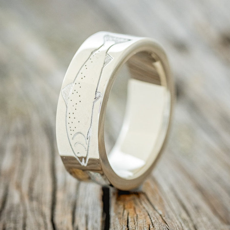Shown here is a custom, handcrafted men's wedding ring featuring a lazer engraved trout with whiskey barrel and fire and ice opal inlays, upright facing left. Additional engraving and inlay options are available upon request.