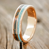 Shown here is "Dyad", a custom, handcrafted men's wedding ring featuring 2 channels with turquoise and patina copper inlays on a 14K gold band, upright facing left. Additional inlay options are available upon request.