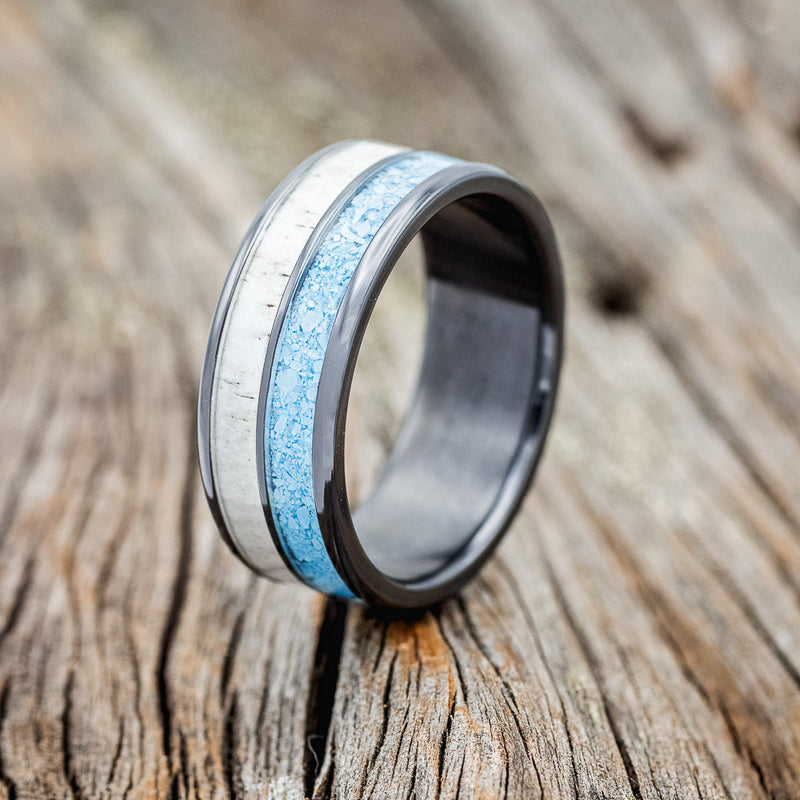 Shown here is "Dyad", a custom, handcrafted men's wedding ring featuring 2 channels with turquoise and antler inlays, shown here on a fire-treated black zirconium band, upright facing left. Additional inlay options are available upon request.