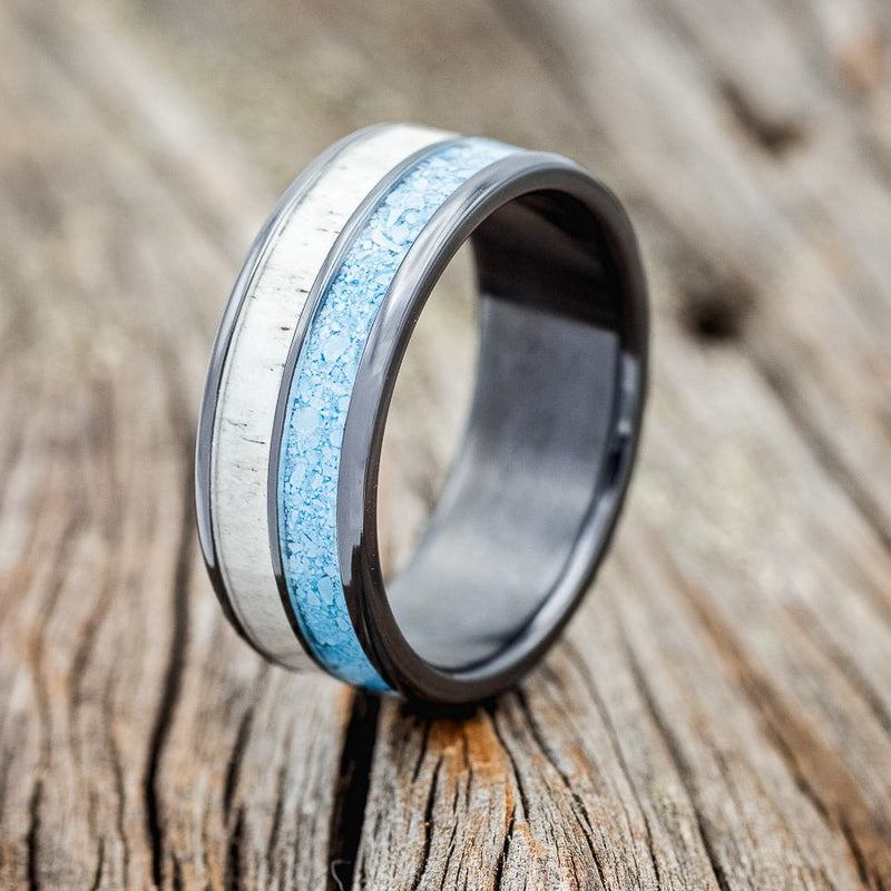 Shown here is "Dyad", a custom, handcrafted men's wedding ring featuring 2 channels with turquoise and antler inlays, shown here on a fire-treated black zirconium band, upright facing left. Additional inlay options are available upon request.