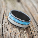 Shown here is "Dyad", a custom, handcrafted men's wedding ring featuring 2 channels with turquoise and antler inlays, shown here on a fire-treated black zirconium band, tilted left. Additional inlay options are available upon request.