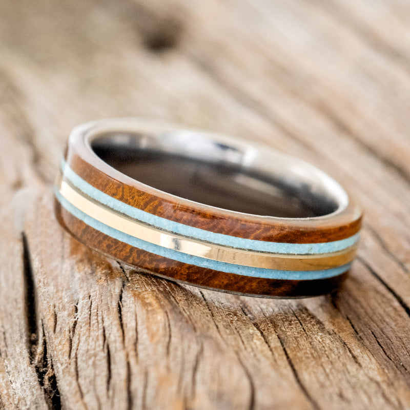 Shown here is "Canyon", a custom, handcrafted men's ring featuring 14K yellow gold and turquoise inlays set between two ironwood overlays, tilted left. Additional inlay and overlay options are available upon request.