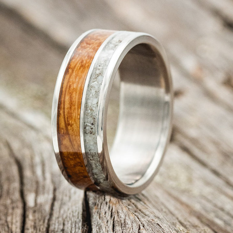 Shown here is "Raptor", a custom, handcrafted men's wedding ring featuring an authentic whiskey barrel stave and elk tooth inlay, shown here on a titanium band, upright facing left. Additional inlay options are available upon request.
