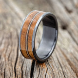 Shown here is "Rainier", a custom, handcrafted men's wedding ring featuring 2 channels with whiskey barrel oak inlays divided by a guitar string, upright facing left. Additional inlay options are available upon request.