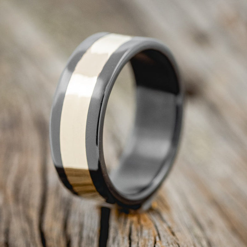 Shown here is "Kalder", a custom, handcrafted men's wedding ring featuring a 14K yellow gold inlay on a wide edge black zirconium band, upright facing left. Additional inlay options are available upon request.