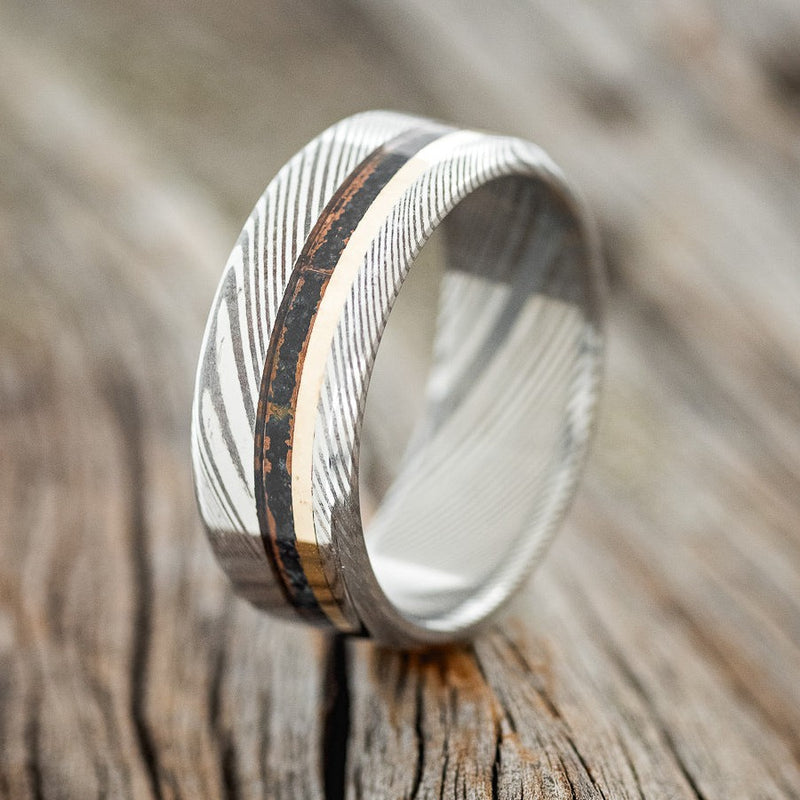 Shown here is "Castor", a custom, handcrafted men's wedding ring featuring patina copper and a 14K yellow gold inlay, shown here on a Damascus steel band, upright facing left. Additional inlay options are available upon request.