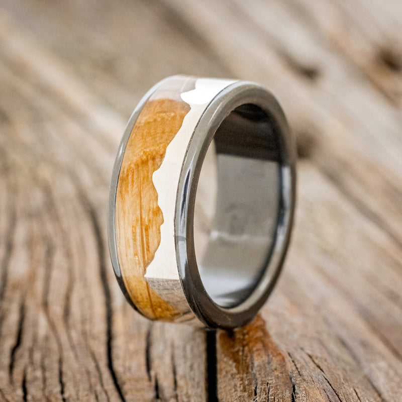 Shown here is "Helios", a custom, handcrafted men's wedding ring featuring a mountain range using pieces of silver and a whiskey barrel oak inlay, upright facing left. Additional inlay options are available upon request.