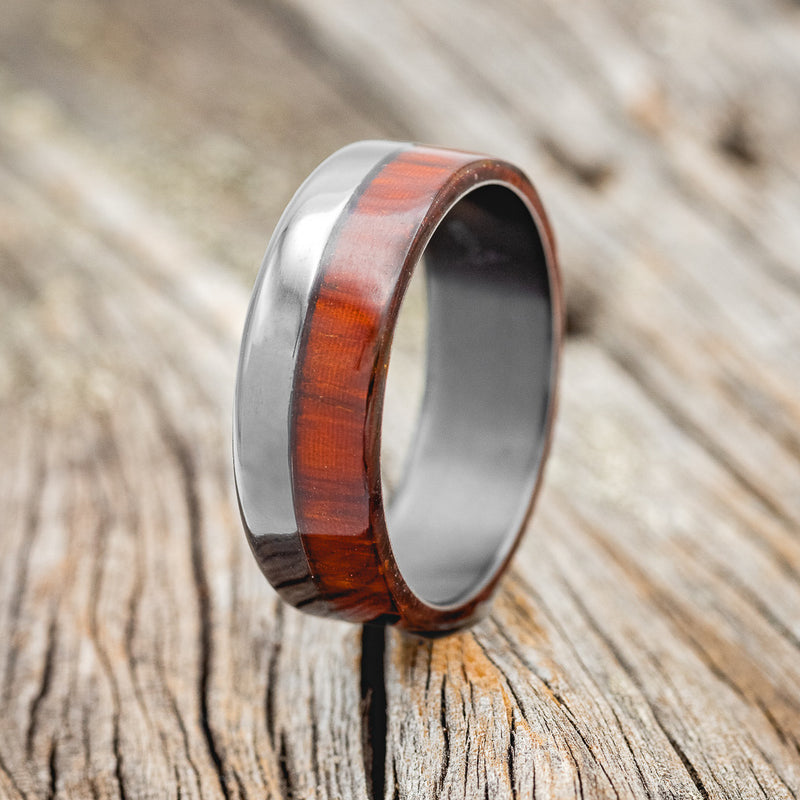 Shown here is "Ledger", a custom, handcrafted men's wedding ring featuring a Padauk wood overlay, upright facing left. Additional inlay options are available upon request.