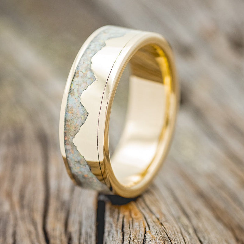 Shown here is "Helios", a custom, handcrafted men's wedding ring featuring a mountain range using pieces of gold and crushed fire & ice opal, upright facing left. Additional inlay options are available upon request.