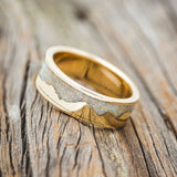 Shown here is "Helios", a custom, handcrafted men's wedding ring featuring a mountain range using pieces of gold and crushed fire & ice opal, tilted left. Additional inlay options are available upon request.
