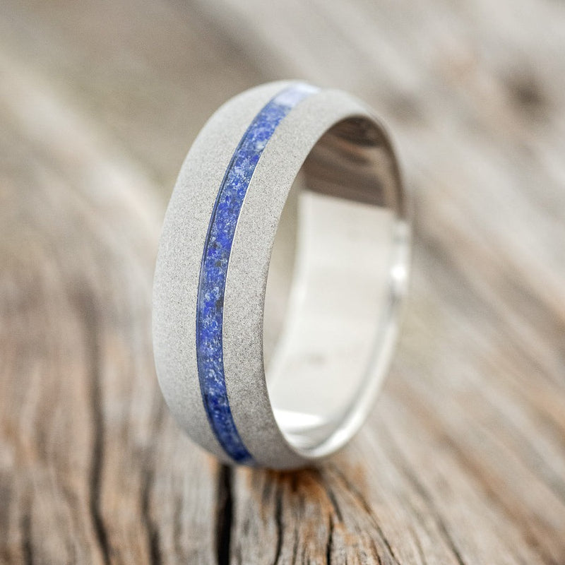 Shown here is "Vertigo", a custom, handcrafted men's domed wedding ring featuring a lapis lazuli inlay with a sandblasted finish, upright facing left. Additional inlay options are available upon request.