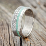 Shown here is "Vertigo", a custom engraved Celtic sailor's knot-patterned men's wedding ring featuring a malachite and opal mixed inlay, upright facing left. Additional inlay options are available upon request.