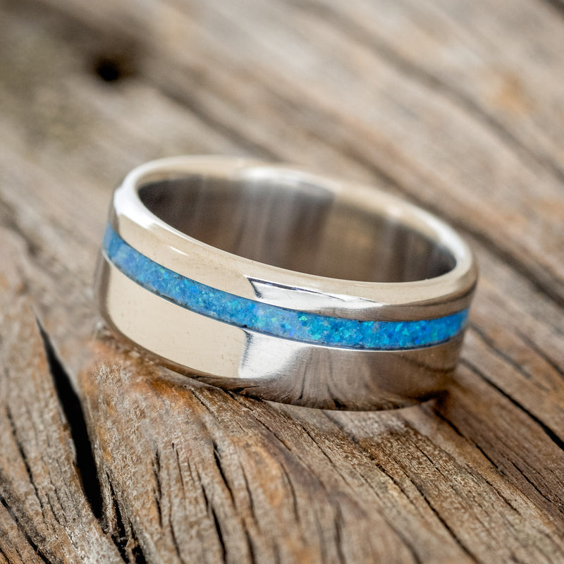 Shown here is "Vertigo", a handcrafted men's wedding ring featuring a blue opal inlay, tilted left.