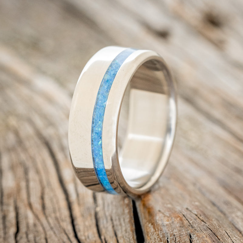 Shown here is "Vertigo", a handcrafted men's wedding ring featuring a blue opal inlay, upright facing left.