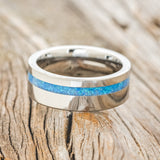 Shown here is "Vertigo", a handcrafted men's wedding ring featuring a blue opal inlay, laying flat.