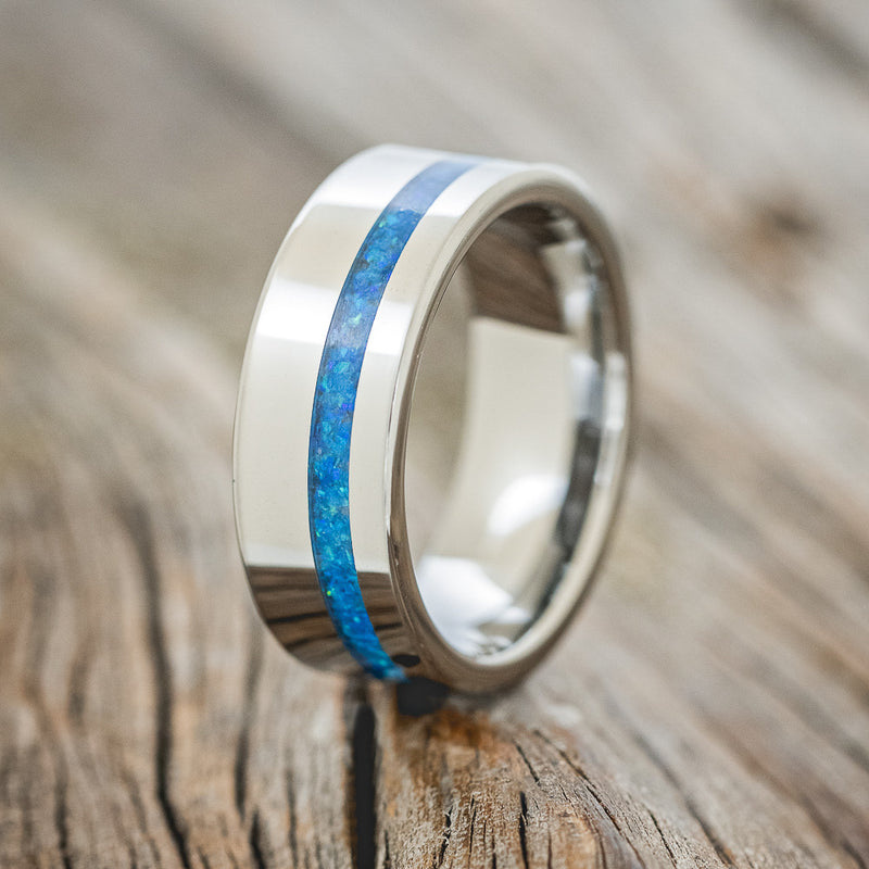 Shown here is "Vertigo", a handcrafted men's wedding ring featuring a blue opal inlay, upright facing left. 