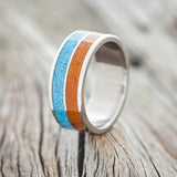 Shown here is "Dyad", a custom, handcrafted men's wedding ring featuring 2 channels with terracotta & turquoise inlays, upright facing left. 