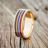 Shown here is "Rio", a custom, handcrafted men's wedding ring featuring 3 channel ring with ironwood and lapis lazuli inlays on a 14K yellow gold band, upright facing left. Additional inlay options are available upon request.