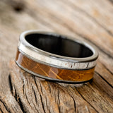 Shown here is "Raptor", a custom, handcrafted men's wedding ring featuring authentic whiskey barrel oak and elk antler on a fire-treated black zirconium band, tilted left. Additional inlay options are available upon request.