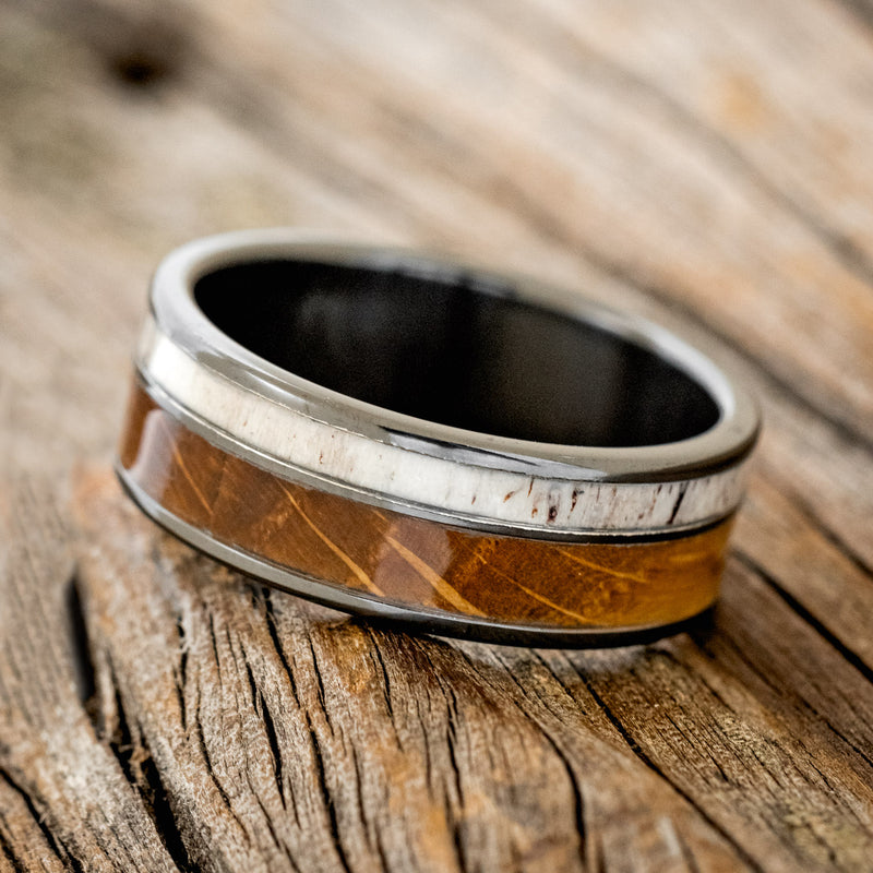 Shown here is "Raptor", a custom, handcrafted men's wedding ring featuring an authentic whiskey barrel stave and elk antler, tilted left. Additional inlay options are available upon request.