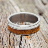 Shown here is "Raptor", a custom, handcrafted men's wedding ring featuring an authentic whiskey barrel stave and elk antler, laying flat. Additional inlay options are available upon request.