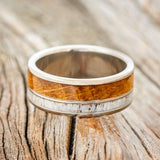 Shown here is "Raptor", a custom, handcrafted men's wedding ring featuring authentic whiskey barrel oak and elk antler inlays, laying flat. Additional inlay options are available upon request.