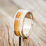 Shown here is "Raptor", a custom, handcrafted men's wedding ring featuring authentic whiskey barrel oak and elk antler inlays, upright facing left. Additional inlay options are available upon request.