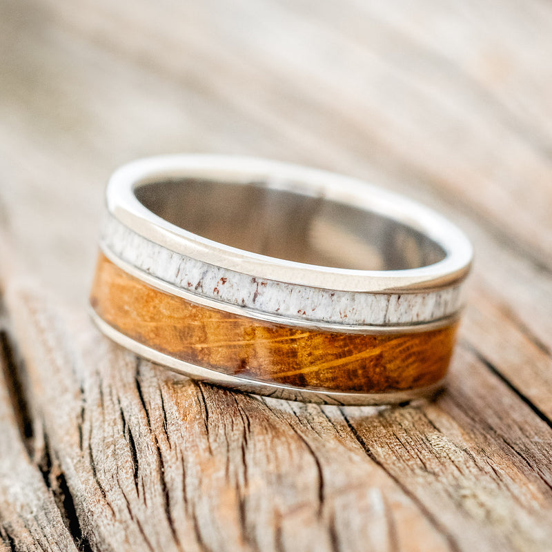 Shown here is "Raptor", a custom, handcrafted men's wedding ring featuring an authentic whiskey barrel stave and elk antler, tilted left. Additional inlay options are available upon request.