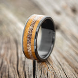 Shown here is "Rainier", a custom, handcrafted men's wedding ring featuring a whiskey barrel oak and antler inlay, upright facing left.