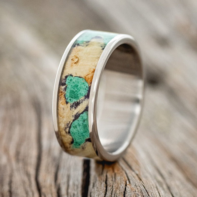 Shown here is "Rainier", a handcrafted men's wedding ring featuring buckeye burl wood with malachite inlays set into the burls, shown here on a titanium band, upright facing left. Additional inlay options are available upon request.
