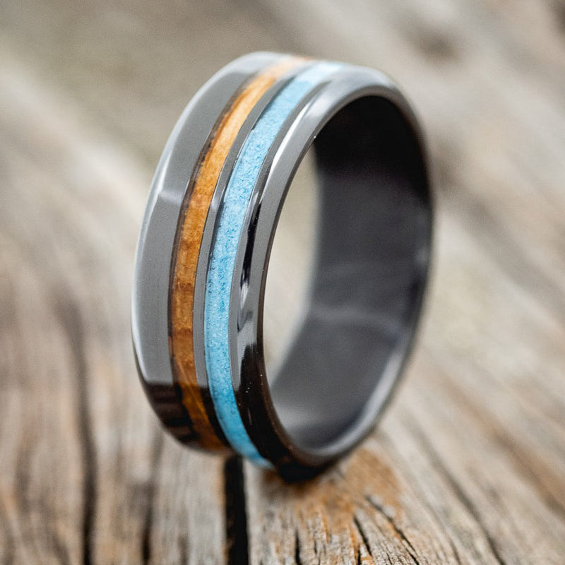 Shown here is "Cosmo", a custom, handcrafted men's wedding ring featuring whiskey barrel oak and turquoise inlays, shown here on a black zirconium band, upright facing left. Additional inlay options are available upon request.