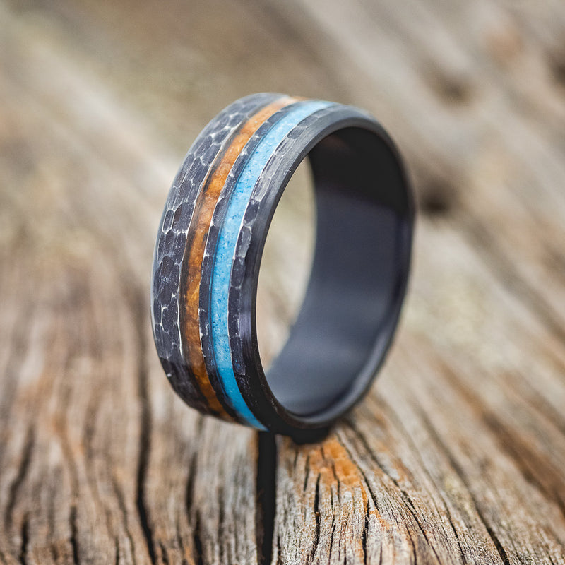 Shown here is "Cosmo", a custom, handcrafted men's wedding ring featuring offset whiskey barrel oak and turquoise inlays, shown here on a hammered black zirconium band, upright facing left. Additional inlay options are available upon request.