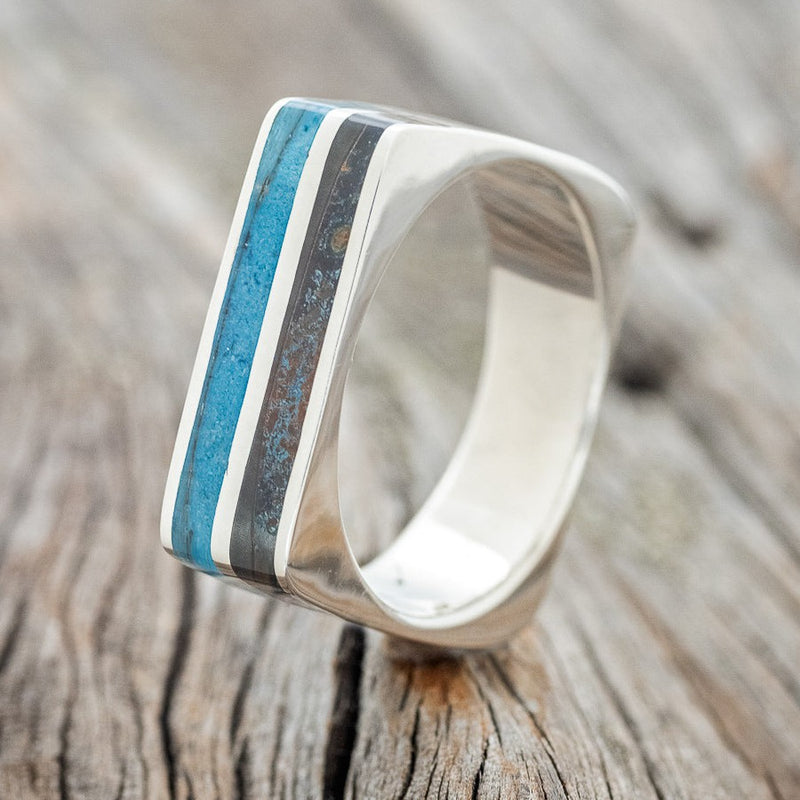 Shown here is "Vega", a custom, handcrafted men's wedding band featuring turquoise and patina copper inlays, upright facing left. Additional inlay options are available upon request.