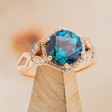 Shown here is "Lucy in the Sky", a halo-style hexagon alexandrite women's engagement ring, on stand facing slightly right, with delicate and ornate details and is available with many center stone options