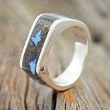 Shown here is "Mesa", a custom, handcrafted men's wedding band featuring buckeye burl wood, with turquoise inlays set into the burls, and an offset black diamond on the side profile, upright facing left. Additional inlay options are available upon request.
