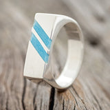 Shown here is "Twain", a custom, handcrafted men's wedding ring featuring two diagonal turquoise inlays, upright facing left. Additional inlay options are available upon request.