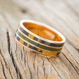 Shown here is "Rio", a custom, handcrafted men's wedding ring featuring 3 channels with white and black ebony wood and moss inlays on a 14K rose gold band, facing right. Additional inlay options are available upon request.