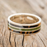 Shown here is "Rio", a custom, handcrafted men's wedding ring featuring 3 channels with white and black ebony wood and moss inlays on a 14K white gold band, laying flat. Additional inlay options are available upon request.