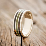 Shown here is "Rio", a custom, handcrafted men's wedding ring featuring 3 channels with white and black ebony wood and moss inlays on a 14K white gold band, upright facing left. Additional inlay options are available upon request.