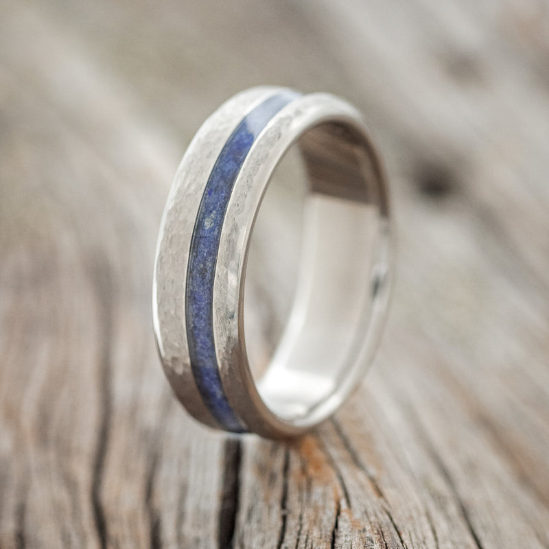 Shown here is "Vertigo", a custom, handcrafted men's wedding ring featuring an offset lapis lazuli inlay with a hammered finish, upright facing left. 