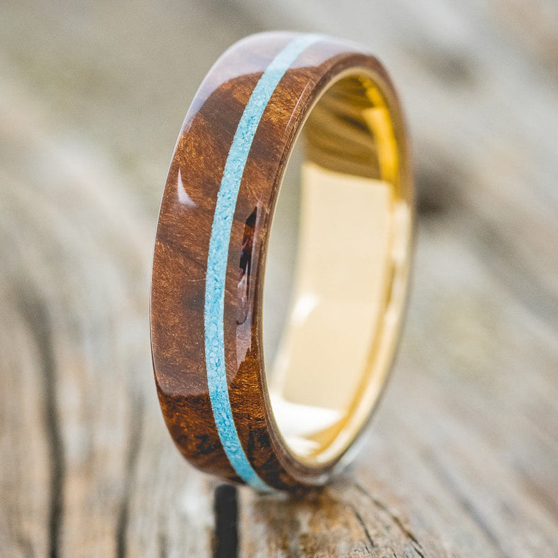 Shown here is "Remmy", a custom, handcrafted men's wedding ring featuring a redwood overlay and an offset turquoise inlay, shown here on a 14K gold band, upright facing left. Additional inlay options are available upon request.